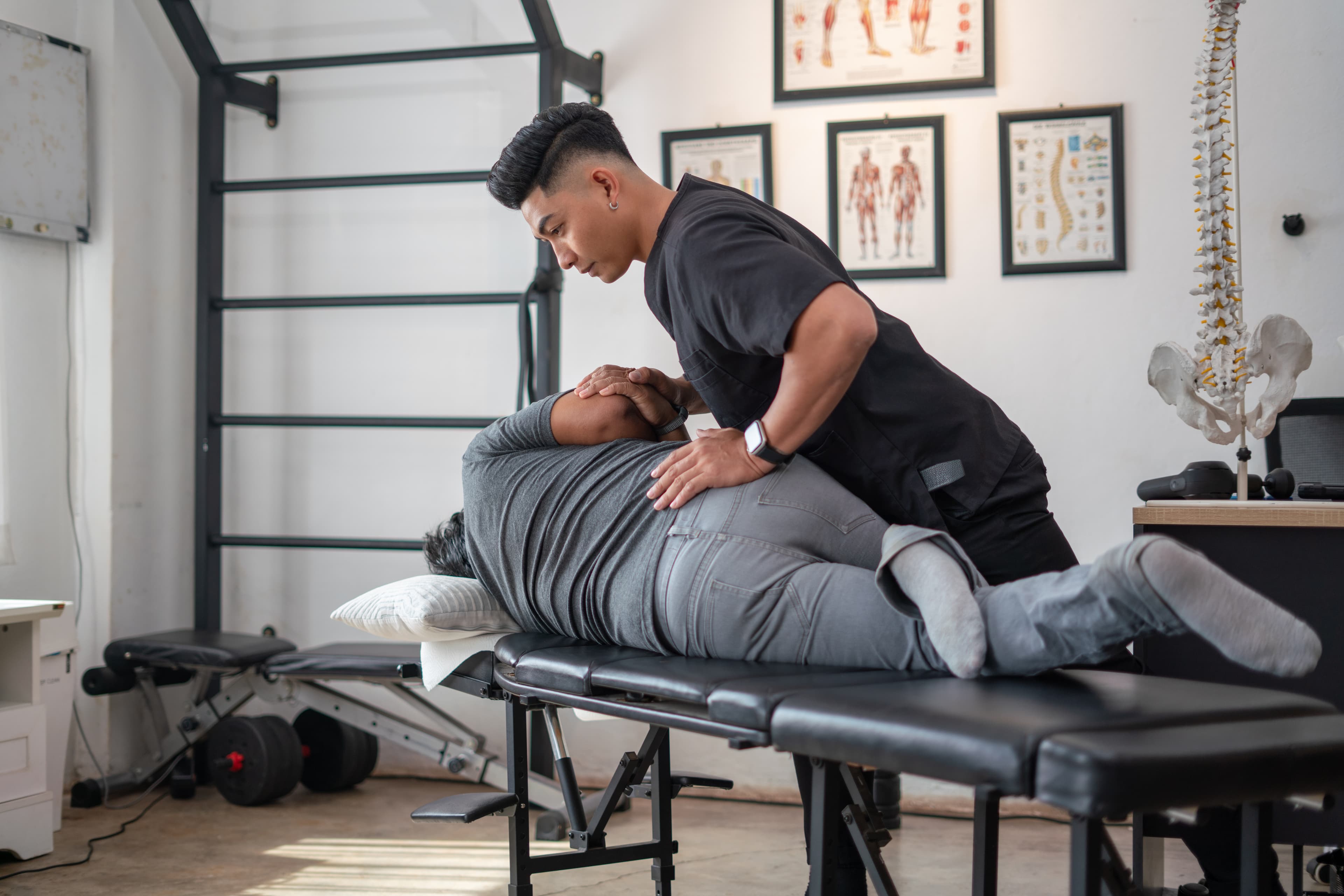 Male chiropractor performing a manual adjustment on a patient lying on a black treatment table.